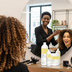 Woman getting her hair styled by a professional in a salon setting with curly hair care products on the counter.