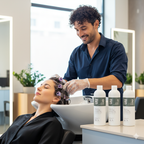 Hairdresser washing a client's hair in a salon with hair care products on a counter.