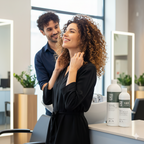 Woman getting her hair styled by a man in a salon with hair products on the counter.
